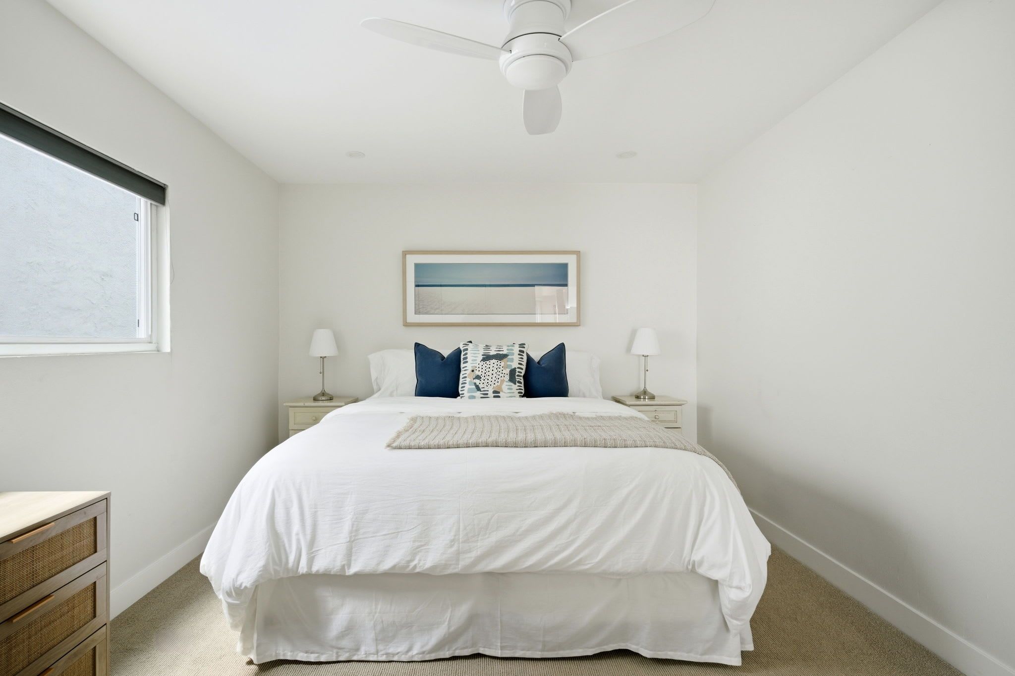 A bedroom with a bed, bedside tables, a ceiling fan, a window, and a framed picture on the wall.