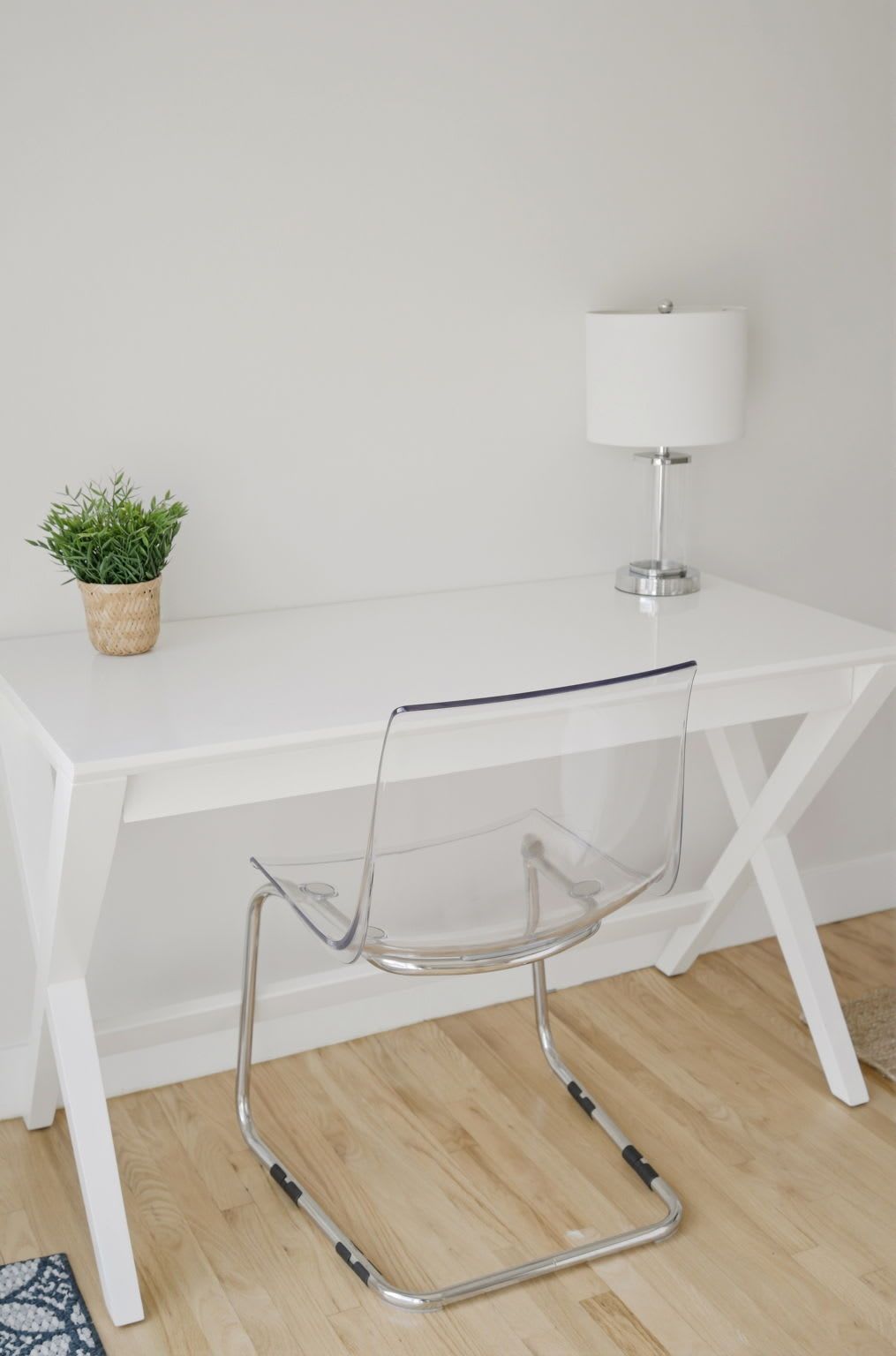 Ein weißer Schreibtisch mit transparentem Stuhl und einer weißen Lampe.