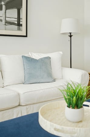A white sofa with a blue pillow, a floor lamp, and a potted plant on a round table. - Coastal Manhattan Beach Home | Walk to Beach & Downtown (Manhattan Beach)