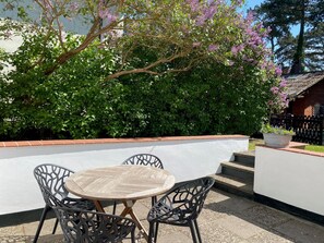 Eine Terrasse im Freien mit einem runden Tisch und vier Stühlen, umgeben von einer niedrigen weißen Mauer und einem blühenden Baum.