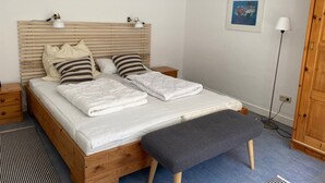 Quarto com cama de madeira, mesas de cabeceira, um banco, abajur e um quadro na parede.