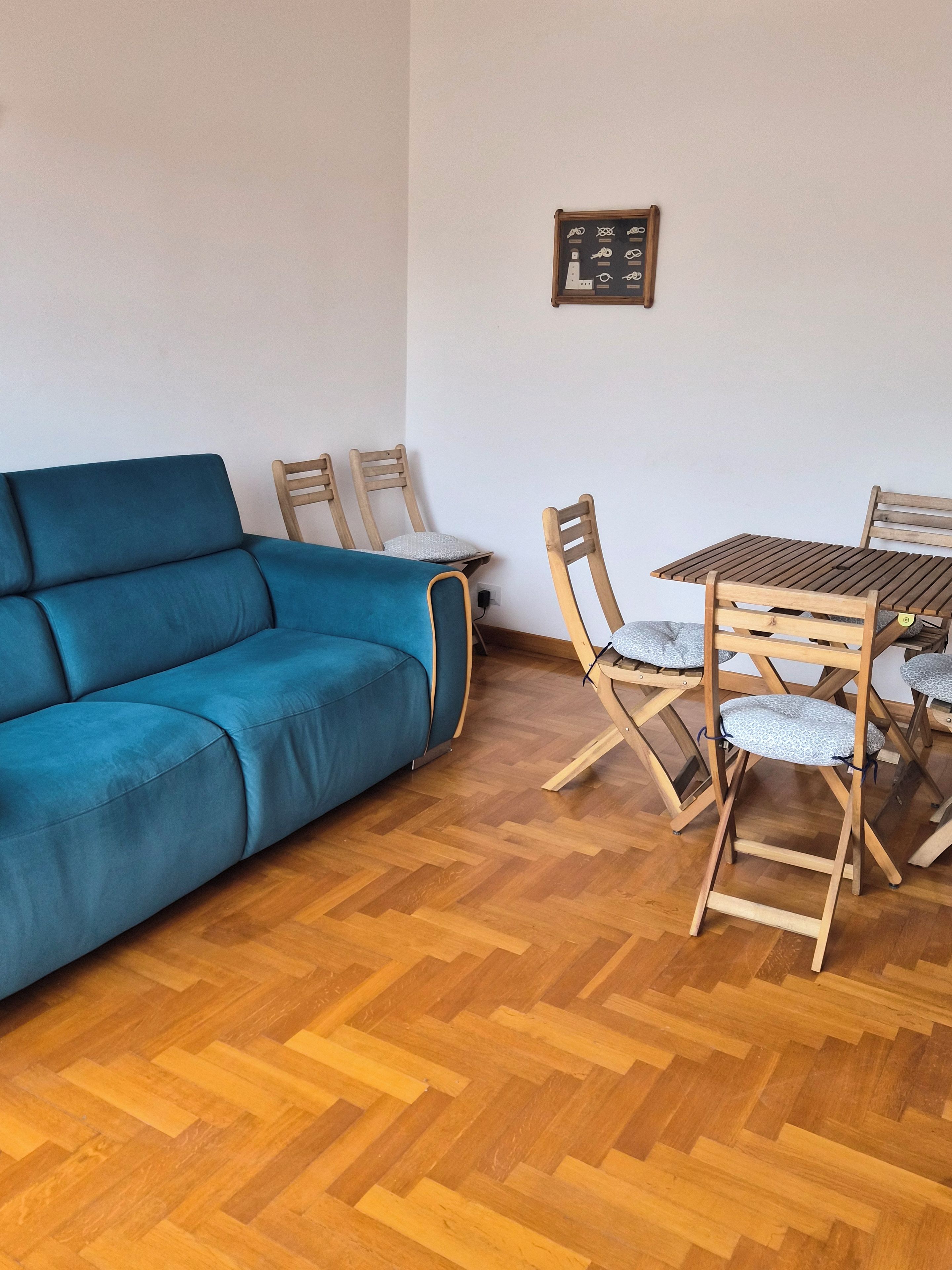 A living room with a blue sofa, wooden chairs, a wooden table, and a herringbone-patterned wooden floor.