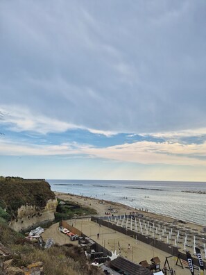 A beach with a sandy shore, umbrellas, and a rocky cliff. - Due Passi di Blu: Your own little oasis of relaxation just a few steps from the sea in Anzio (Anzio)