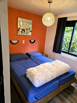 Una habitació amb un llit, una obra d'art penjada a la paret, una làmpada penjolant i una finestra amb vista a vegetació.