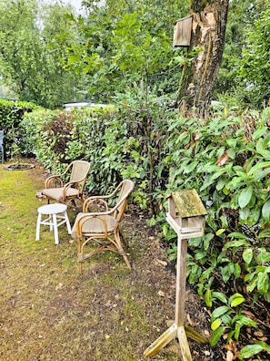 A garden with wicker chairs, a wooden birdhouse, and lush greenery. - The Veluwe Nest (Epe)