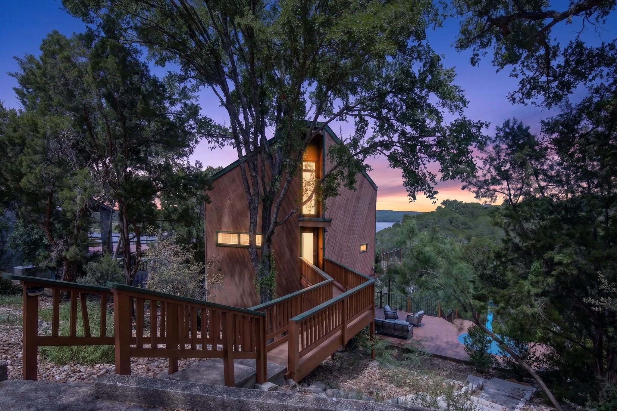 A wooden cabin with a staircase, surrounded by trees and a clear sky.