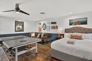 A hotel room with a bed, a table tennis table, a sofa, and a ceiling fan. - *New* Hill Country Treehouse Retreat | Pool, Hot Tub & Lake Travis Views ⛰️🌊 (Spicewood)