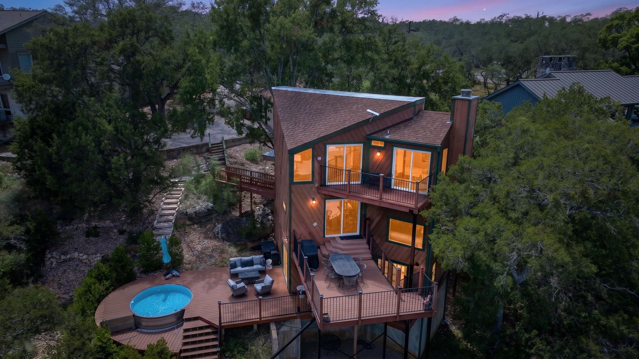 A multi-level wooden house with a deck, outdoor seating, and a swimming pool.