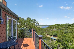 A wooden deck with a metal railing overlooking a lake and forested hills.