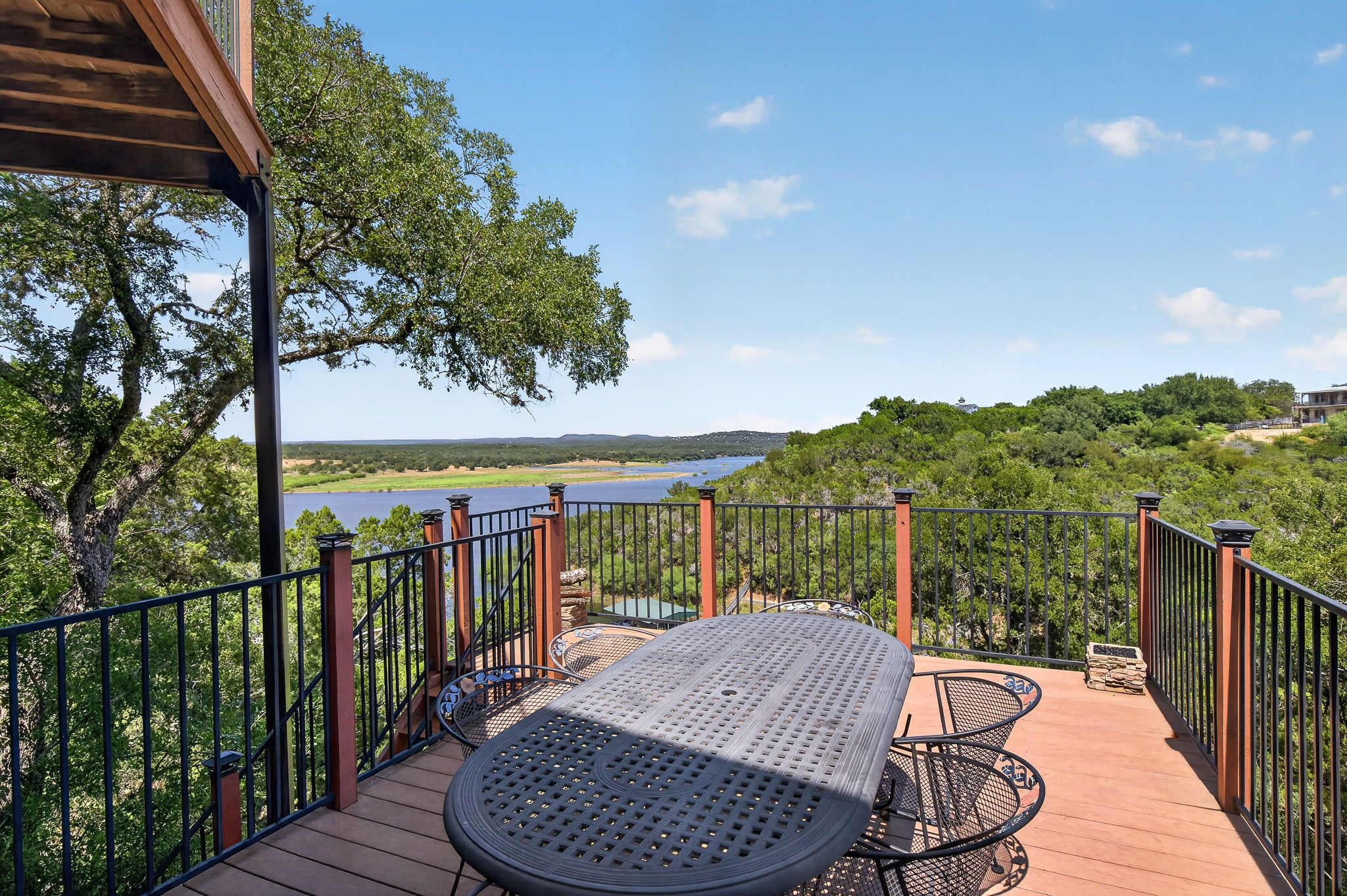 A deck with a table and chairs overlooking a lake and forested hills.