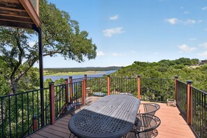 A deck with a table and chairs overlooking a lake and forested hills. - *New* Hill Country Treehouse Retreat | Pool, Hot Tub & Lake Travis Views ⛰️🌊 (Spicewood)