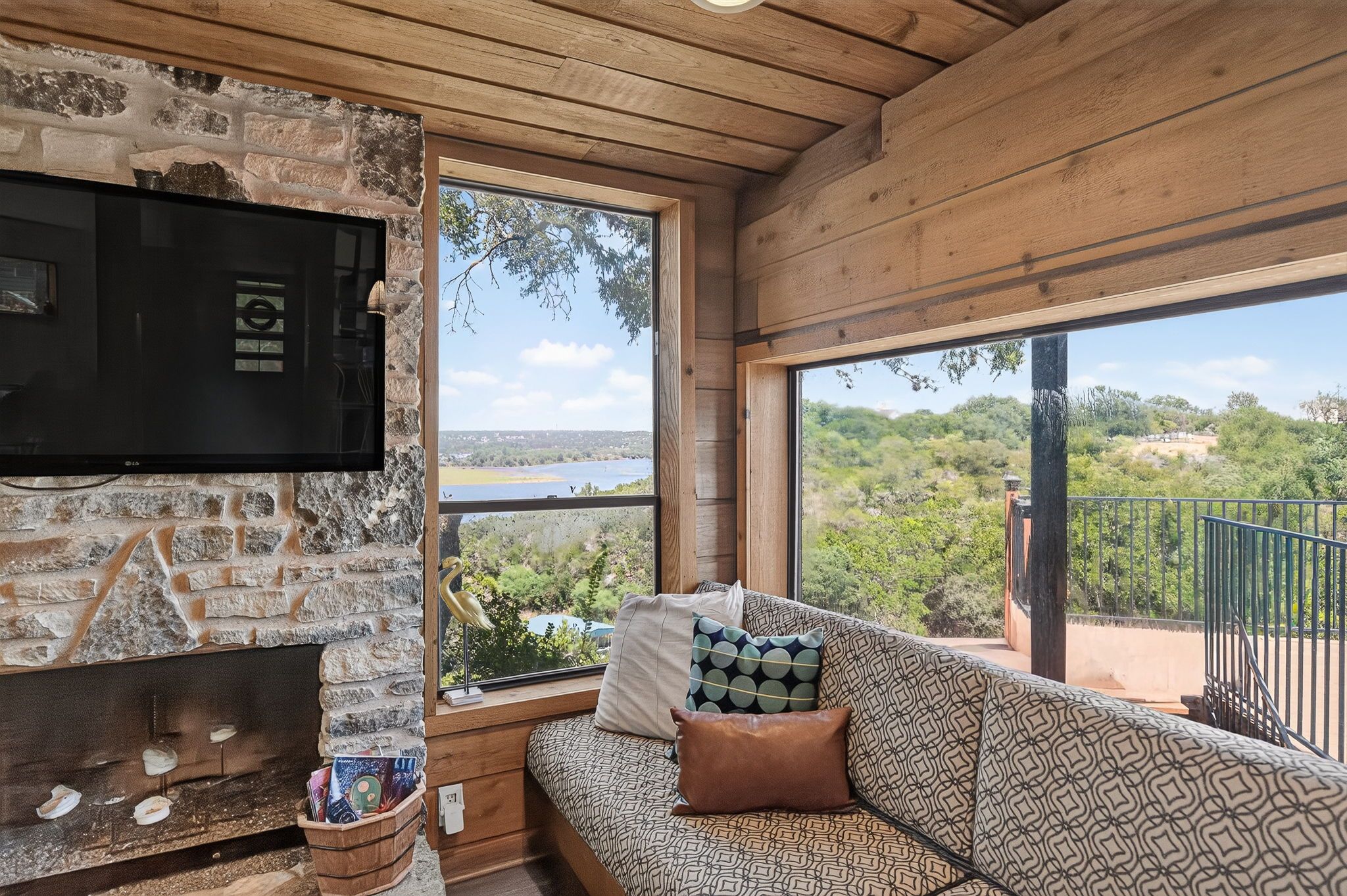Un área de estar acogedora con chimenea de piedra, televisor de pantalla plana y sofá con cojines estampados.
