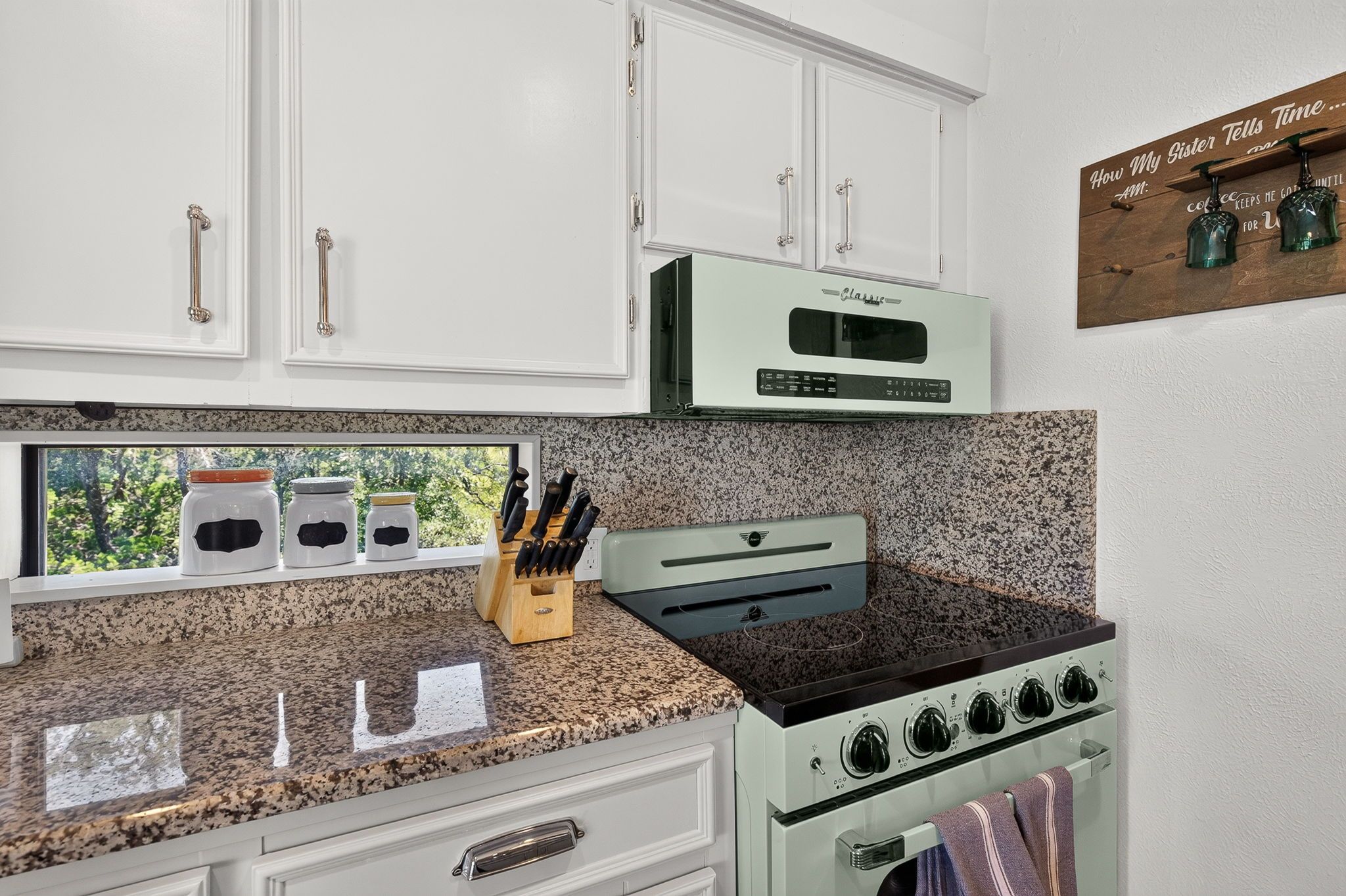A kitchen with white cabinets, a classic range, and a window with a view of trees.