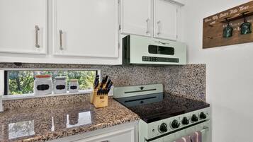 A kitchen with white cabinets, a classic range, and a window with a view of trees.