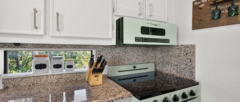 Una cocina con armarios blancos, una estufa clásica y un ventanal con vistas a árboles.