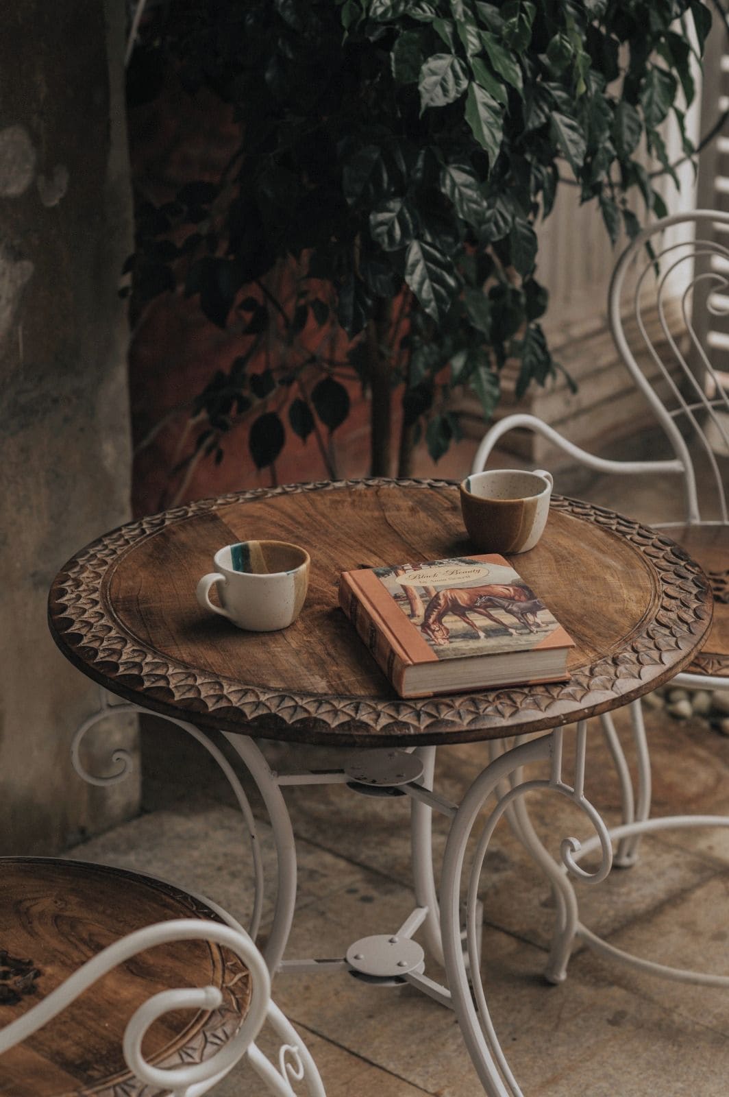 Une table ronde en bois, sur laquelle se trouvent un livre et deux tasses, entourée de chaises en métal.