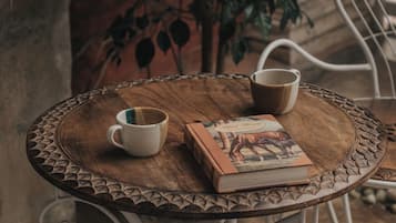 Une table ronde en bois, sur laquelle se trouvent un livre et deux tasses, entourée de chaises en métal.