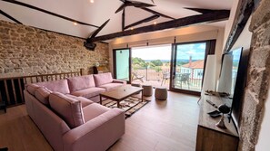 A living room with a stone wall, a pink sofa, a wooden coffee table, and a balcony with a view.