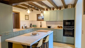 A kitchen with light green cabinets, a marble countertop, a built-in oven, and pendant lighting.