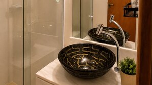 A modern bathroom with a glass shower enclosure, a vanity with a black bowl sink, and a wooden door. - Loft Perequê 50m from the beach • Garage with 600 Mbps Wi-Fi (Ilhabela)