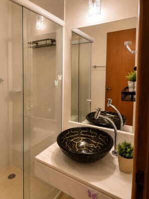 Un baño moderno con cabina de ducha de vidrio, un lavamanos con pileta negra y una puerta de madera.