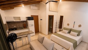 A compact room with a kitchenette, a bed, a sofa, and a fan. - Loft Perequê 50m from the beach • Garage with 600 Mbps Wi-Fi (Ilhabela)