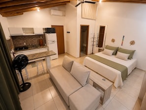 Una habitación compacta con kitchenette, una cama, un sofá y un ventilador.