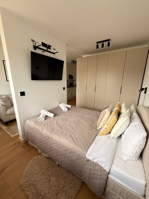Ein Schlafzimmer mit einem Bett, einem an der Wand befestigten Fernseher, einem Kleiderschrank und einem Sofa.