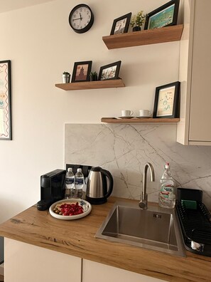 Cozinha com bancada de mármore, pia, chaleira e torradeira. Há quadros em molduras nas prateleiras acima da bancada.