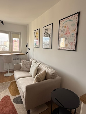 Ein Wohnzimmer mit einer Couch, einem Sessel, einer Stehlampe und einem Fenster mit Blick auf Gebäude.
