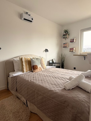 Quarto com cama, mesas de cabeceira, ar-condicionado na parede e janela com vista.