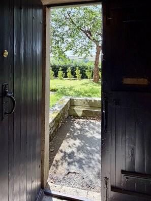 An open wooden door leading to a paved area with a stone wall and a tree. - The West Wing Sleeps 5 With Parking (Barnard Castle)