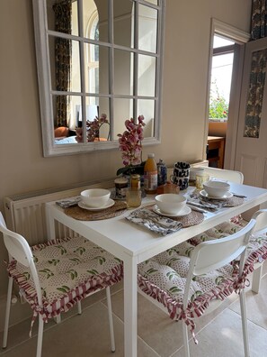 A dining area with a white table set for four, surrounded by white chairs with patterned cushions. - The West Wing Sleeps 5 With Parking (Barnard Castle)