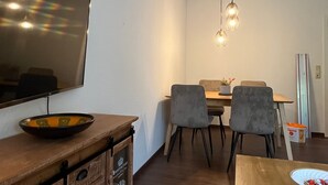 Uma sala de estar moderna com televisão de tela plana, móveis de madeira, um espaço de refeições com cadeiras e um lustre.