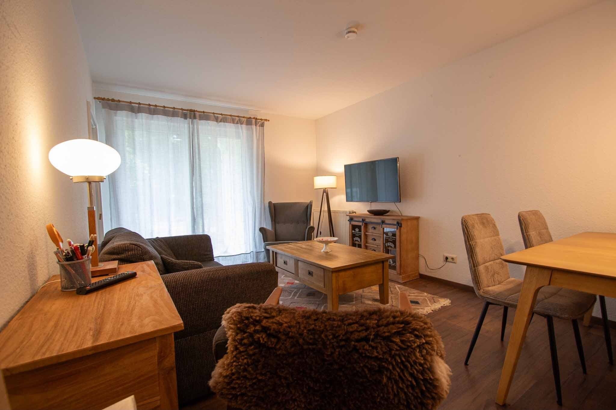 Una sala de estar amoblada con un sofá, una mesa de madera, un televisor y un comedor con sillas.
