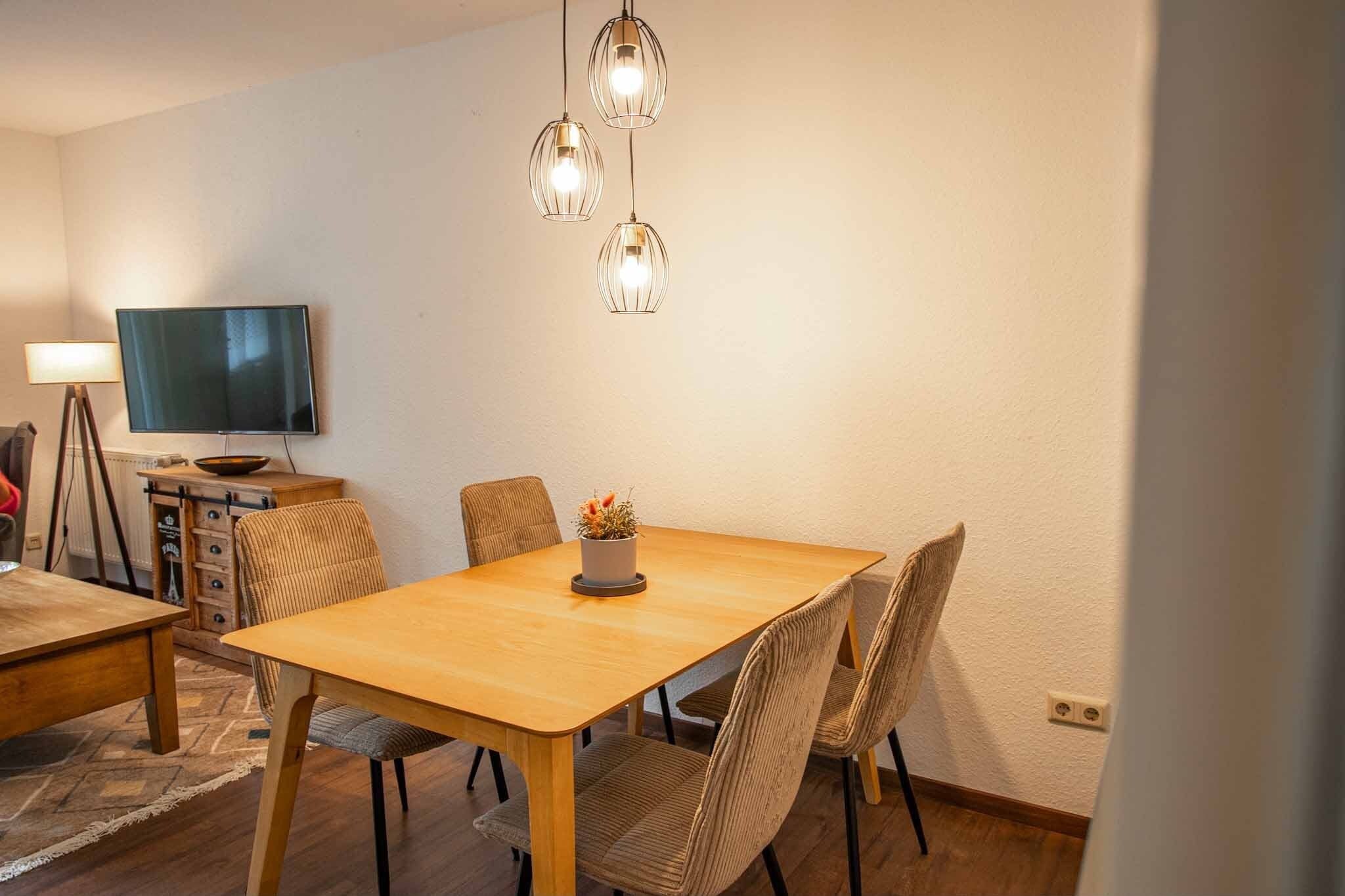 Un espace repas avec une table et des chaises en bois, un téléviseur posé sur un meuble et des luminaires suspendus.