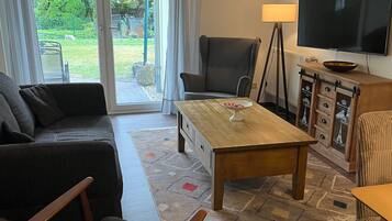 Ett vardagsrum med en soffa, fåtölj, soffbord, TV och utsikt genom en glasdörr.