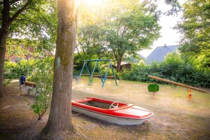 A park with a swing set, a seesaw, a boat, and a bench.
