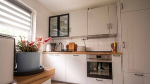 Una cuina moderna amb armaris blancs, forn integrat i finestra amb persianes.