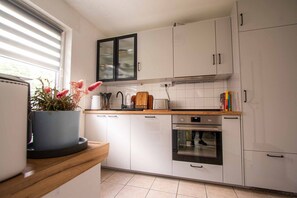 Une cuisine moderne avec des meubles blancs, un four encastré et une fenêtre équipée de stores.