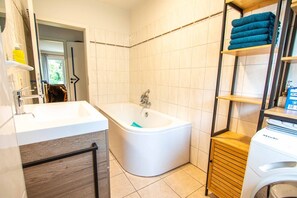 Ein Badezimmer mit einer Badewanne, einem Waschbecken, einem Spiegel und einem Ablagefach mit Handtüchern.