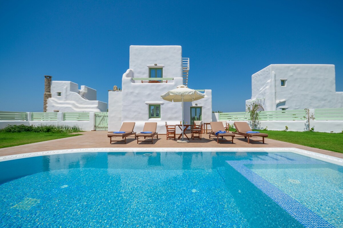 A pool area with lounge chairs and a building with white walls and green windows.