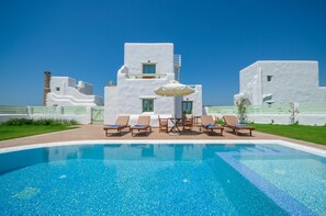 A pool area with lounge chairs and a building with white walls and green windows. - My Villa Naxos (Naxos)