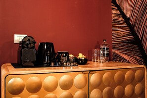 Una kitchenette con cafetera, hervidor, un tazón de galletas y una botella de agua sobre una encimera de madera.