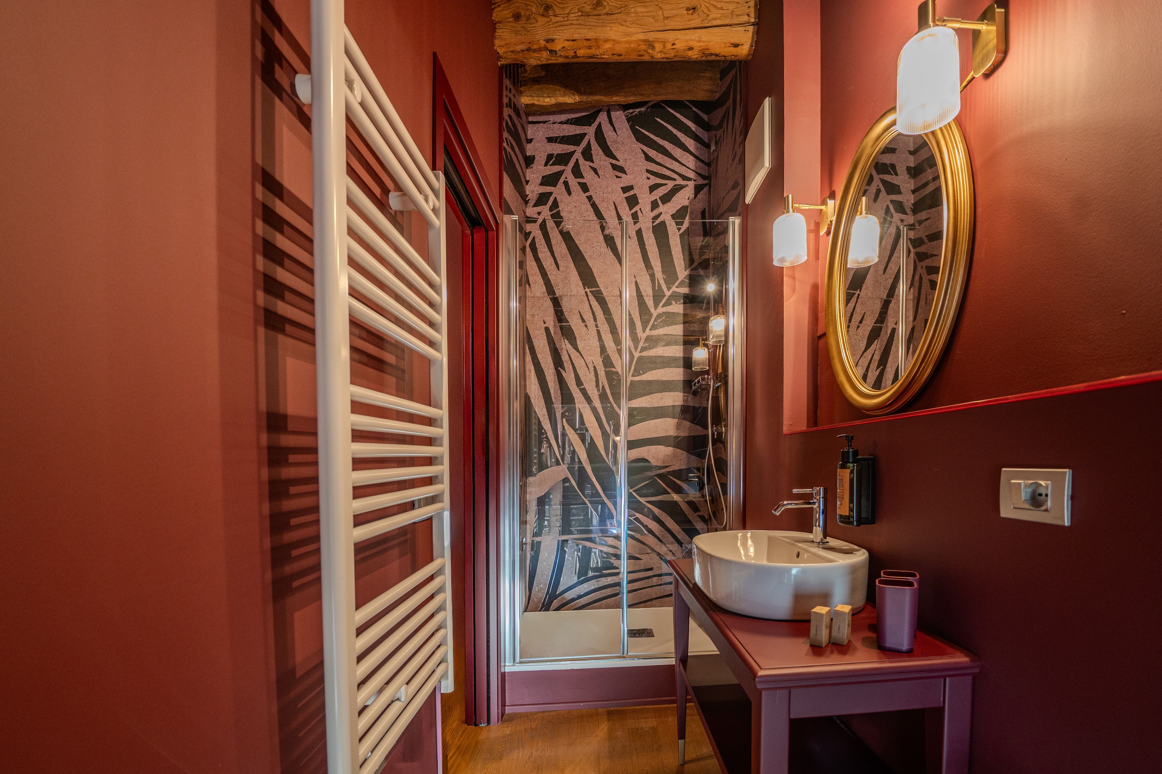 Une salle de bain avec un lavabo blanc, un miroir et une douche dotée d’un rideau de douche orné de motifs de feuilles.