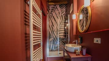 Une salle de bain avec un lavabo blanc, un miroir et une douche dotée d’un rideau de douche orné de motifs de feuilles.