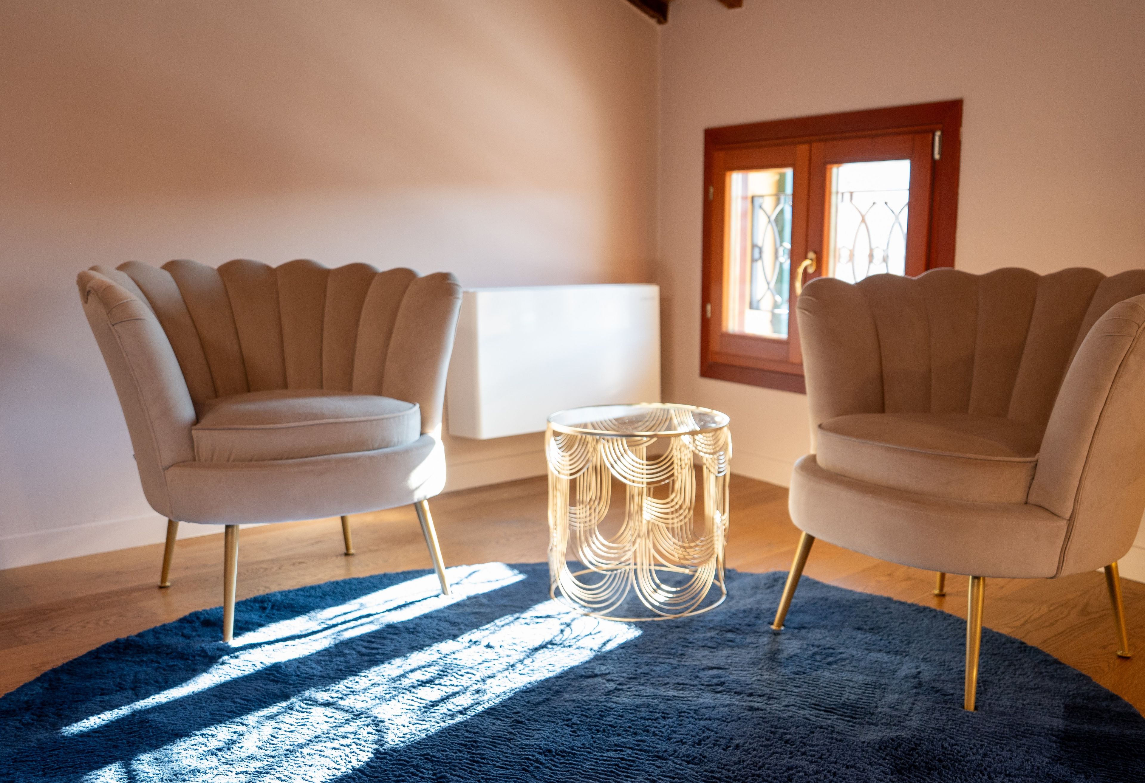 Deux fauteuils disposés de part et d’autre d’une table ronde, un tapis bleu sur le sol et une fenêtre donnant sur l’extérieur.