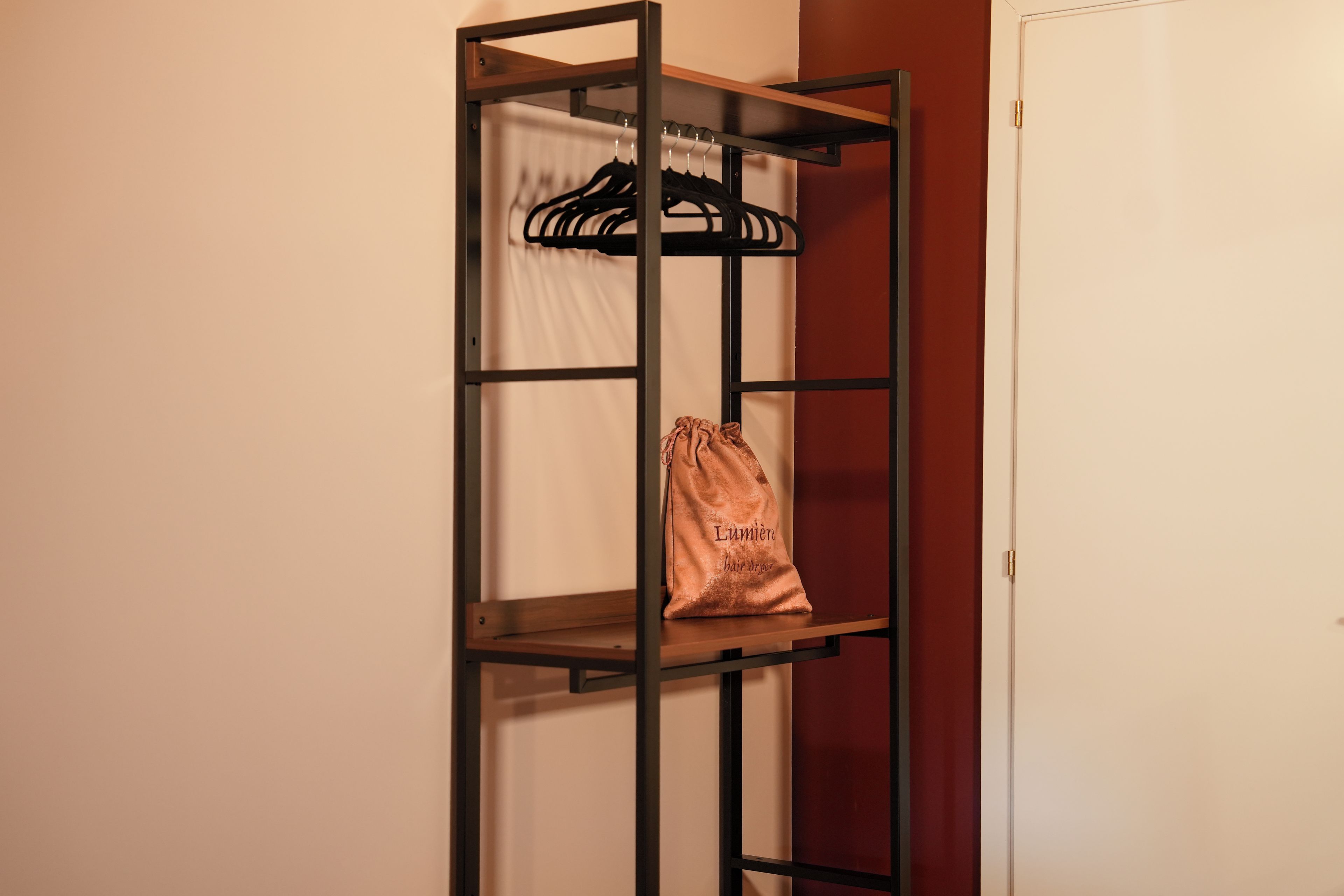 Ein Metallregal mit einer Kleiderstange und einer Tasche mit dem Aufdruck 'Lumiere Haartrockner'.