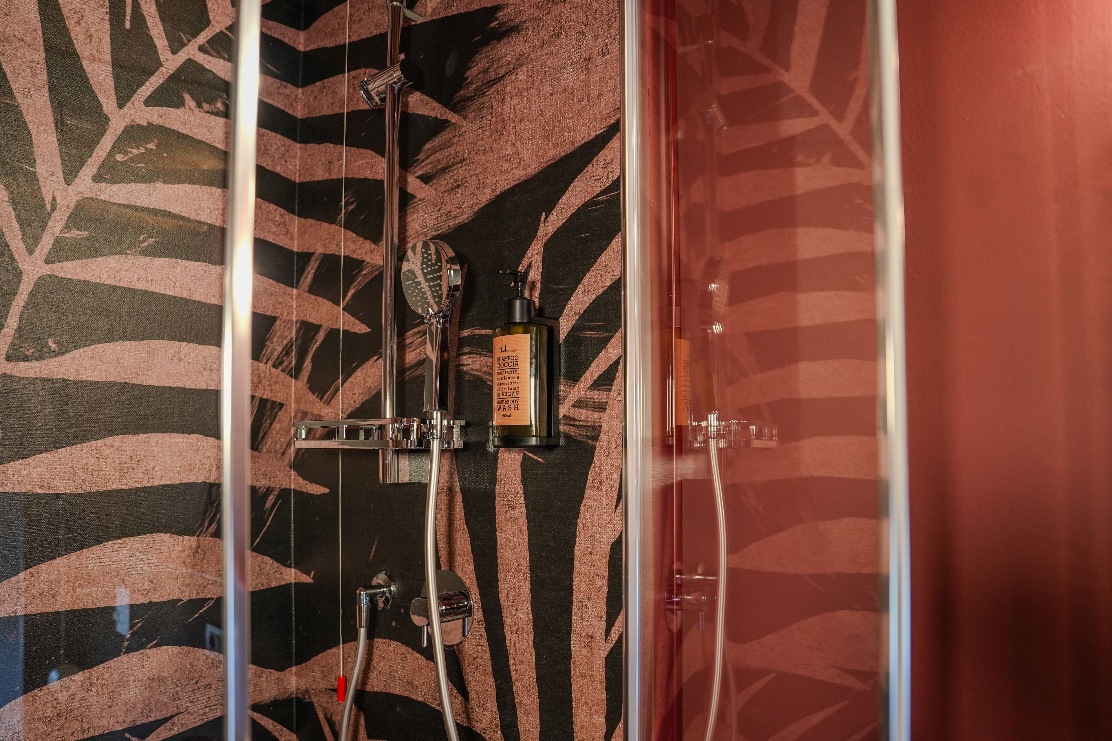 Eine Dusche mit einem Wandmuster aus schwarzen und braunen Blättern, einer Handbrause und einer Shampoo-Flasche.
