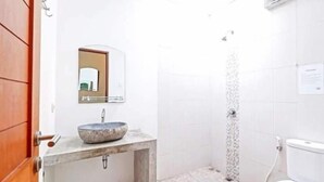 A bathroom with a stone sink, a mirror, a shower, and a toilet. - Castaway Hostel (Badung)